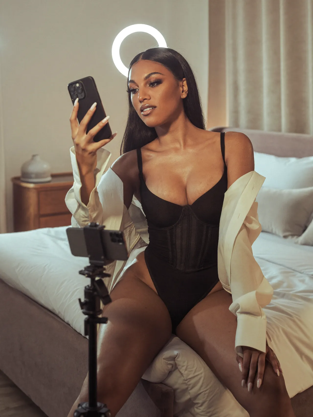 A creator checks her phone on a tripod, ring light on, in her studio bedroom.