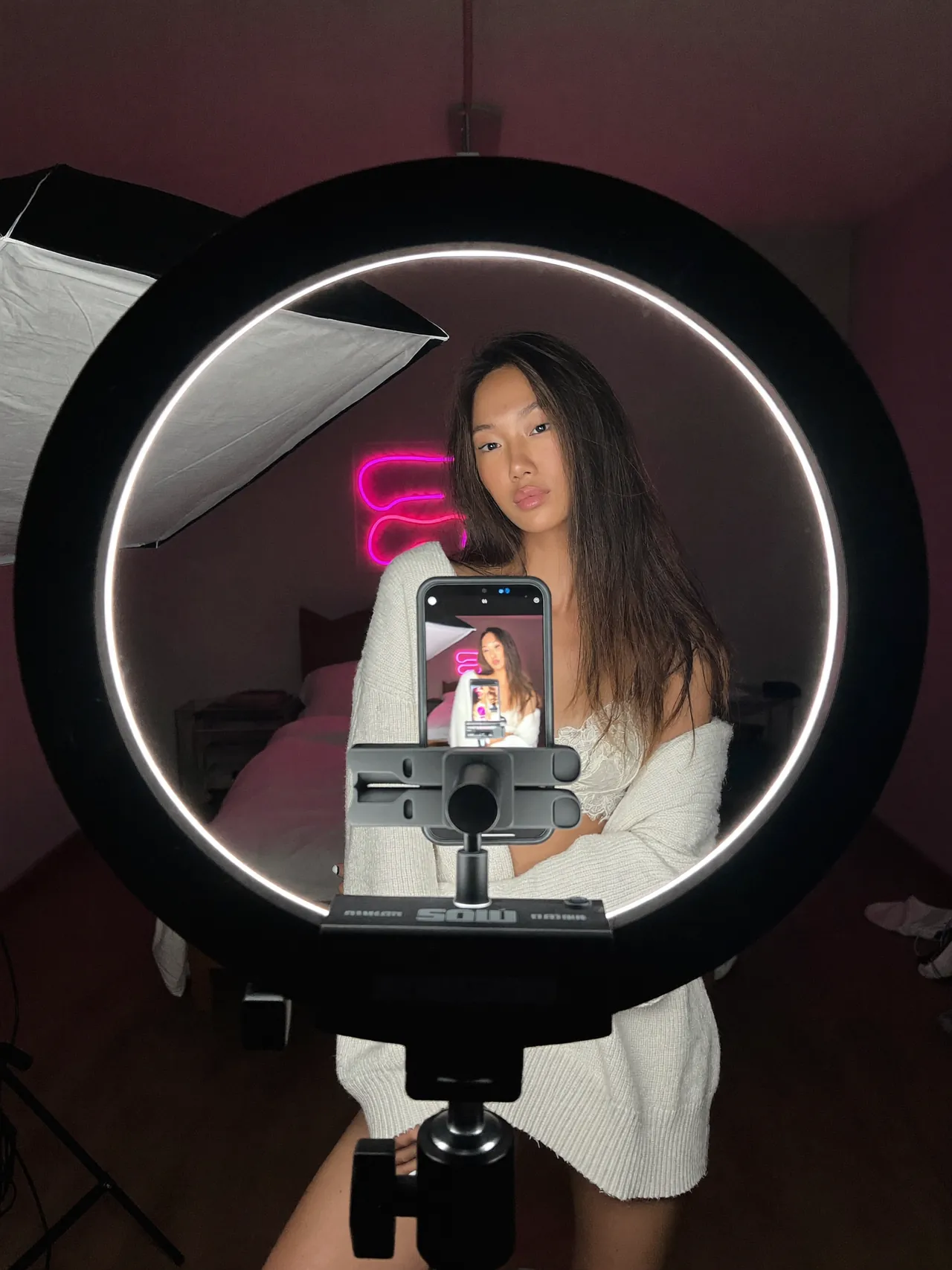A creator adjusts a ring light in front of her phone on a tripod, in a bright room.